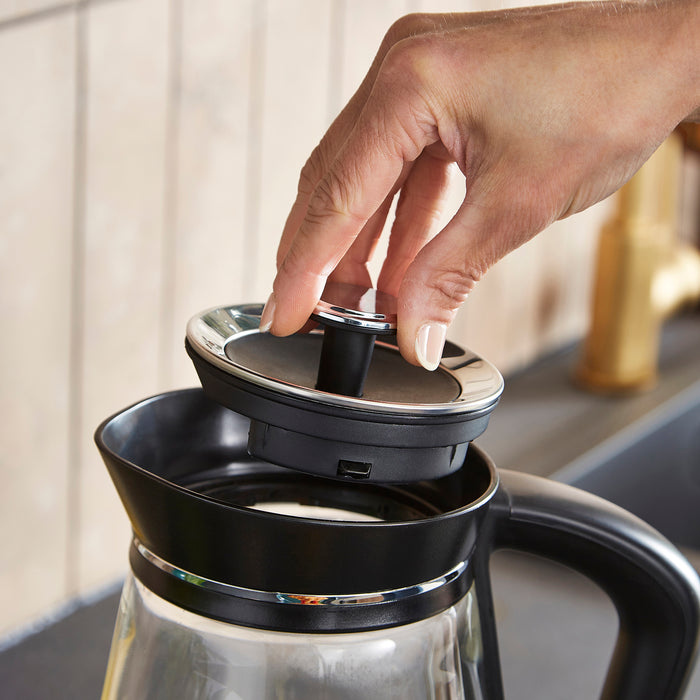 Hand placing a lid on a glass coffee maker with a blurred background
