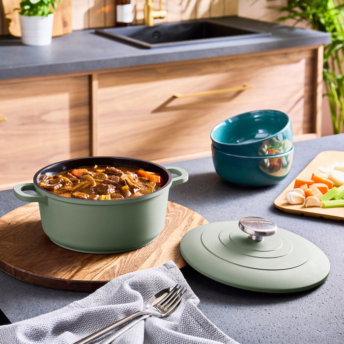 Green casserole dish with food on a kitchen counter, surrounded by kitchen items.