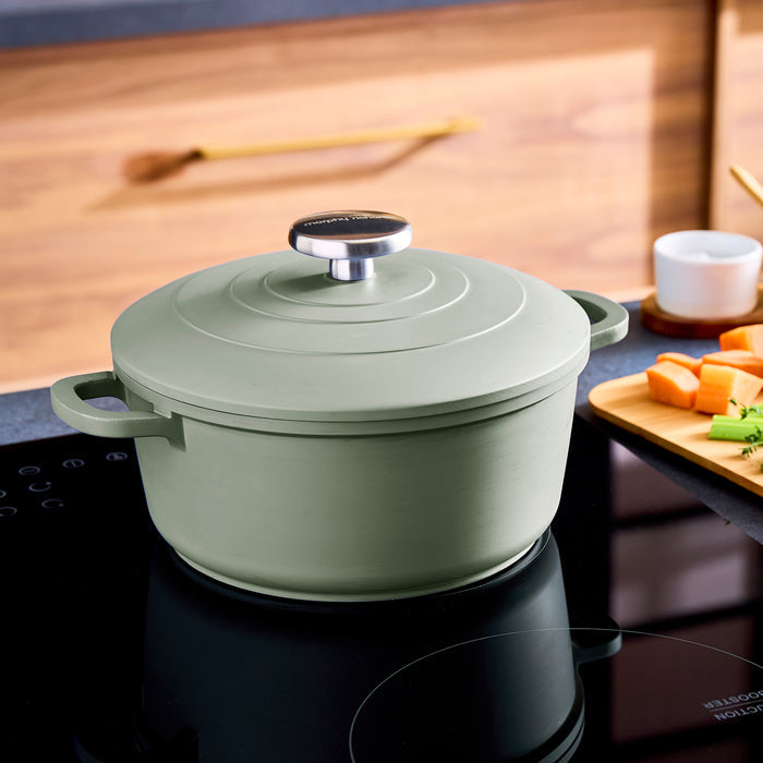 Green casserole pot on a stovetop with a wooden cutting board in the background.
