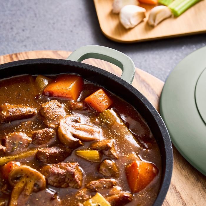 Stew with meat, carrots, and mushrooms in a black pot on a wooden board.