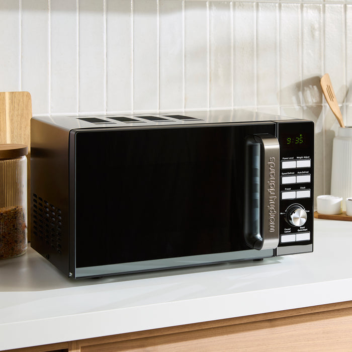 Black microwave oven on a kitchen counter with a white tiled wall background
