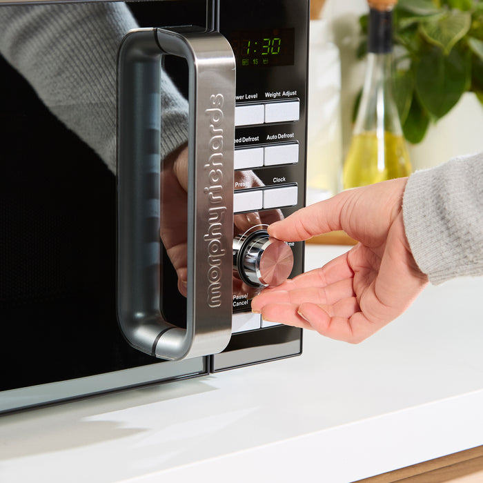 Hand adjusting a digital microwave oven control panel.