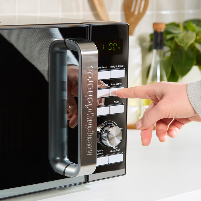 Person using a digital microwave oven with a hand pressing buttons.
