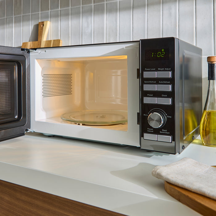 Microwave oven on a kitchen counter with a tiled wall in the background