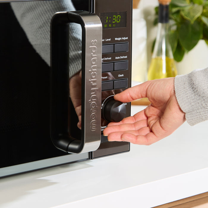 Person using a microwave with a digital display and control panel.
