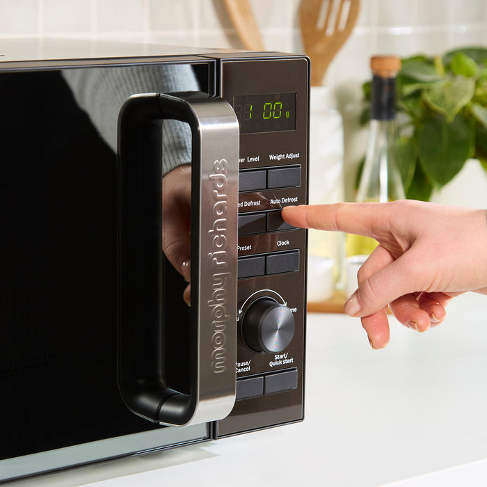 Hand pressing a button on a microwave oven with a blurred kitchen background
