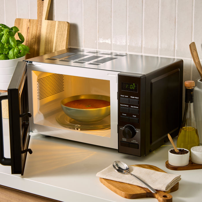 Microwave oven with a bowl of soup inside on a kitchen counter.
