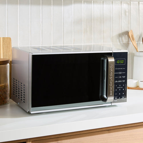 Stainless steel microwave oven on a kitchen counter with a white tiled wall in the background.