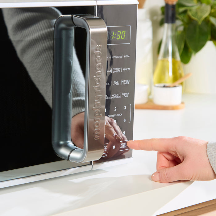 Hand opening a microwave oven on a kitchen counter.