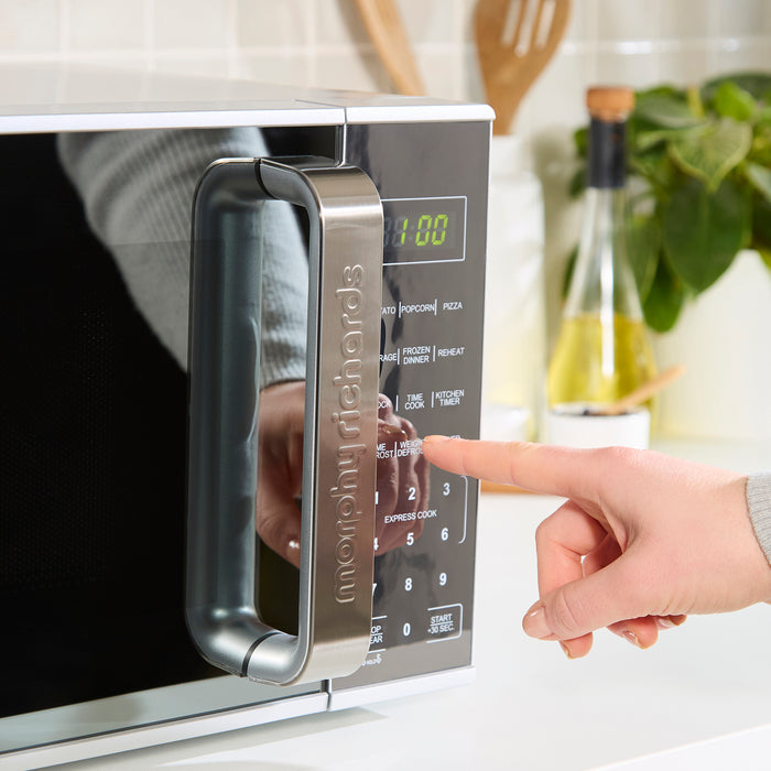 Person using a modern microwave oven with digital display and control panel.