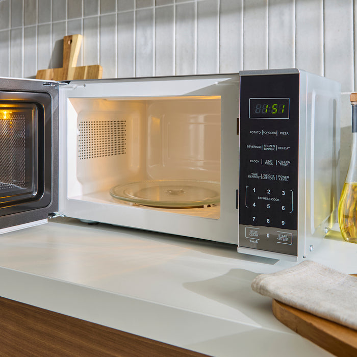 Open microwave on a kitchen counter with tiled wall in the background
