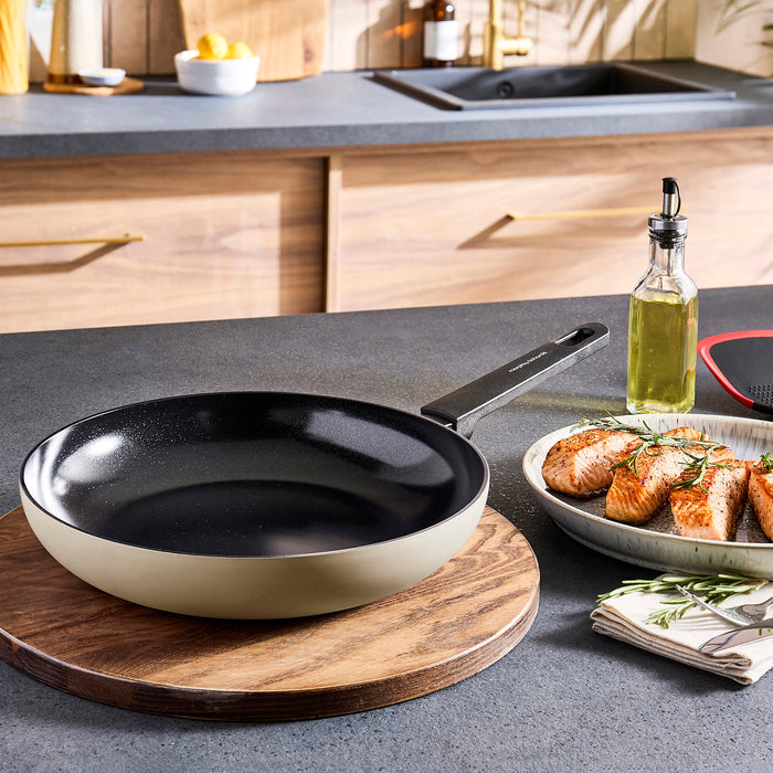 Creamfrying pan on a wooden trivet with a plate of food in a kitchen setting