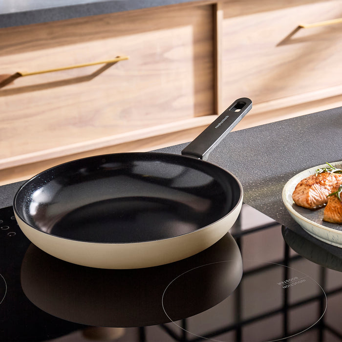 Cream frying pan on a stovetop with a plate of food in the background