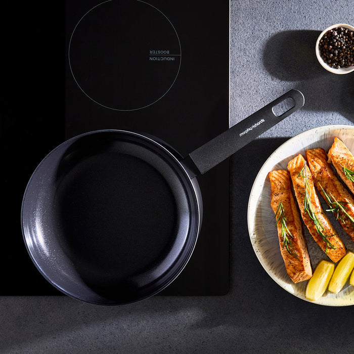 Black frying pan on a stovetop with a plate of food next to it