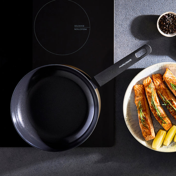 Black frying pan on a stovetop with a plate of food next to it