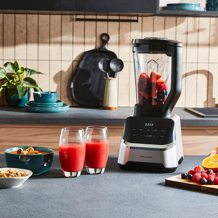 Kitchen blender with fruits, glasses of juice, and bowls on a kitchen counter.