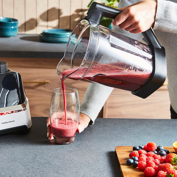 Person pouring a smoothie from a blender into a glass on a kitchen counter.