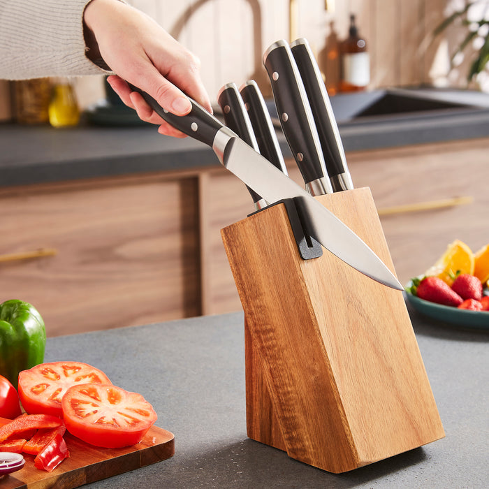 Set of knives in a wooden block on a kitchen counter with vegetables.
