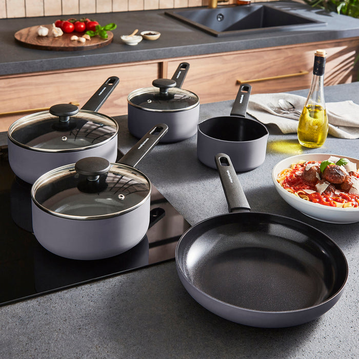 Set of cookware including pots, pans, and a frying pan on a kitchen counter with a bowl of pasta.