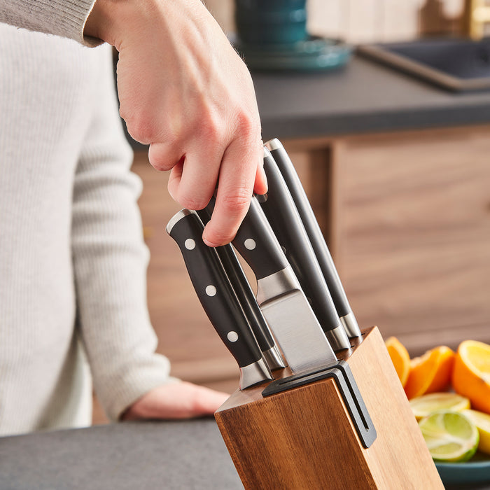 Person holding a set of knives in a wooden block with fruits in the background