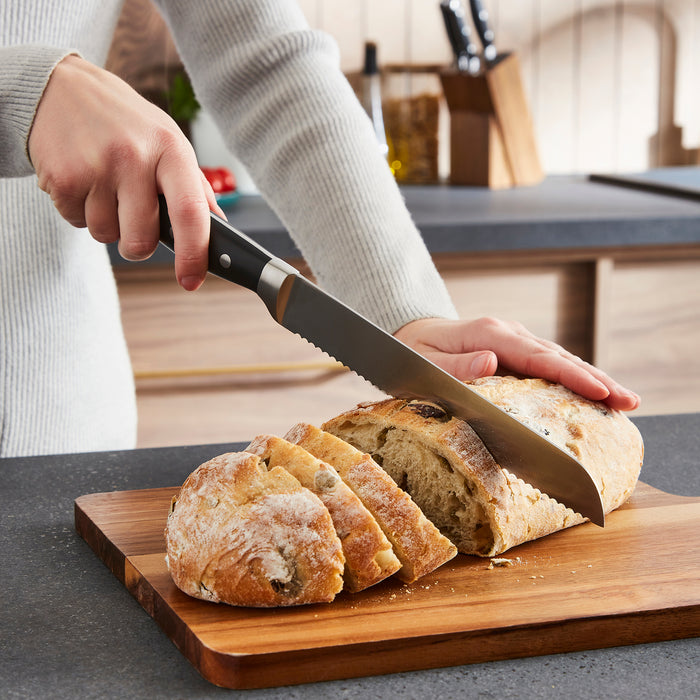 Person slicing bread on a wooden cutting board with a knife.