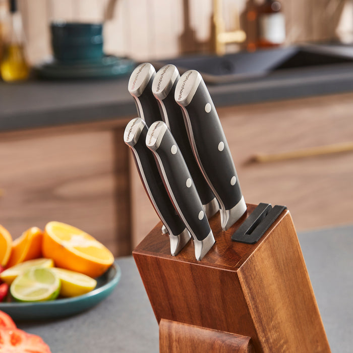 Set of knives in a wooden block on a kitchen counter with fruits in the background