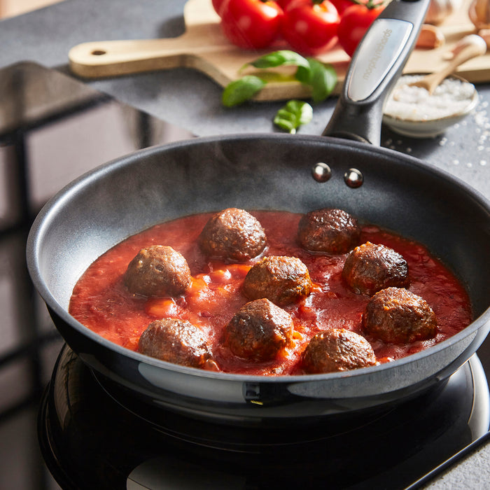 Frying pan with meatballs in tomato sauce on a stovetop