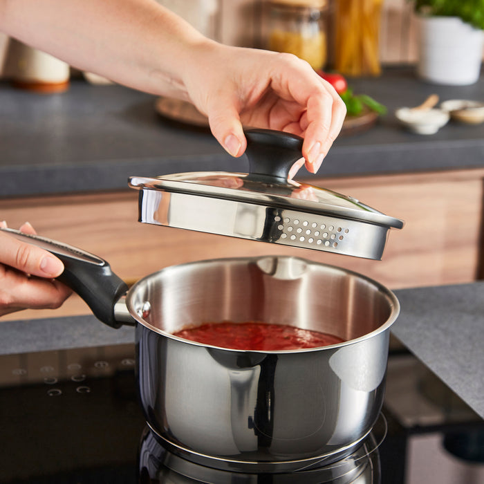 Person holding a lid over a pot of food on a stove in a kitchen.