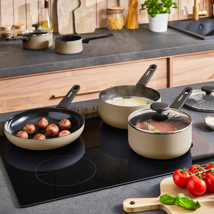 Set of cookware on a stovetop with food being prepared in a kitchen setting.