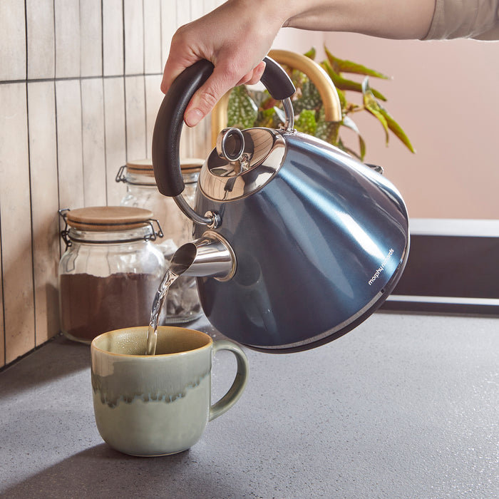 Person pouring water from a blue kettle into a mug on a kitchen counter.