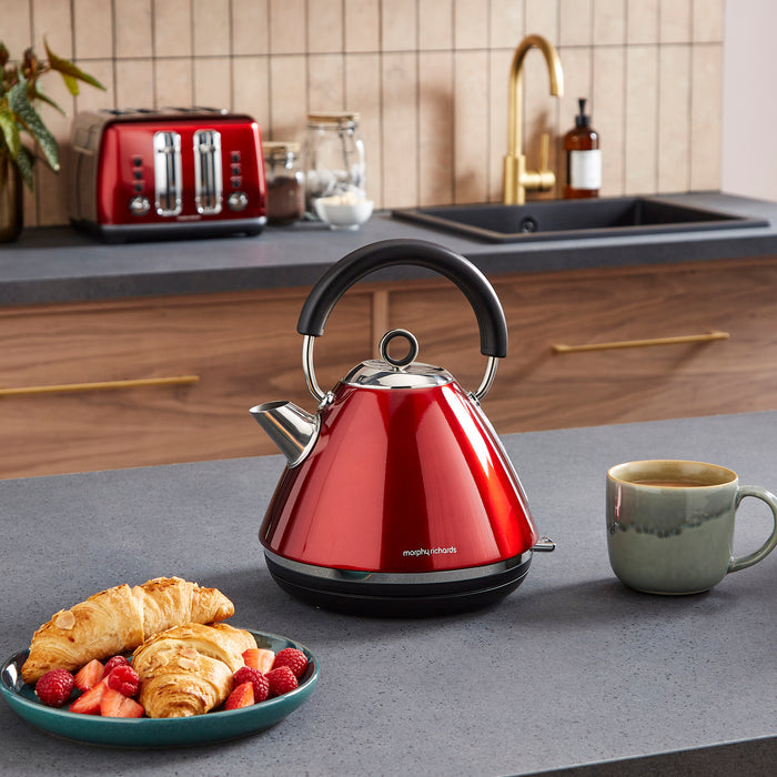 Red kettle on a kitchen counter with a plate of pastries and a mug.