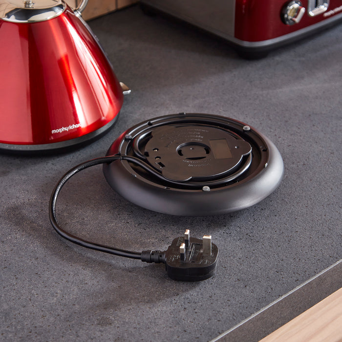 Black electric hot plate with plug on a gray countertop, next to a red kettle.