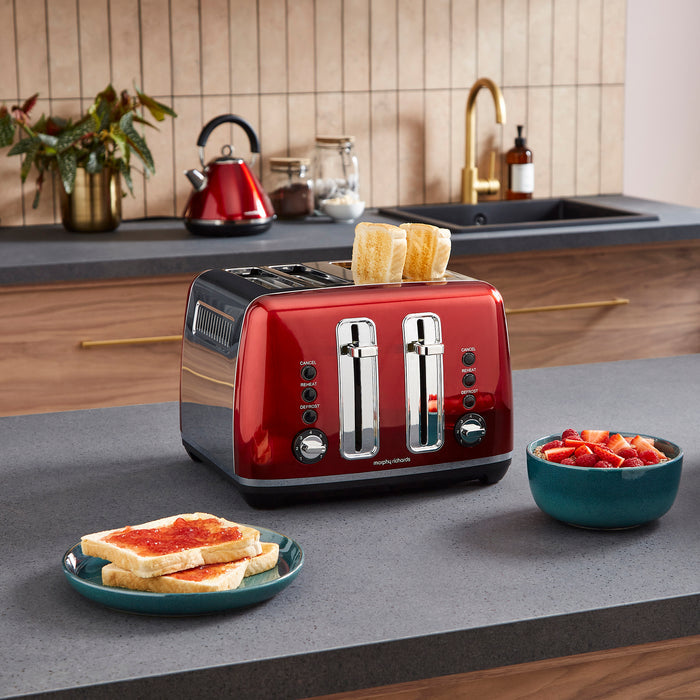Red toaster with slices of bread on a kitchen counter with a bowl of fruit and a plate of toast.