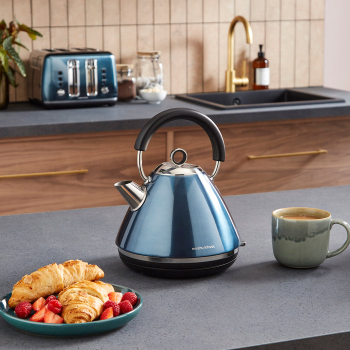 Blue kettle on a kitchen counter with a mug and plate of food.