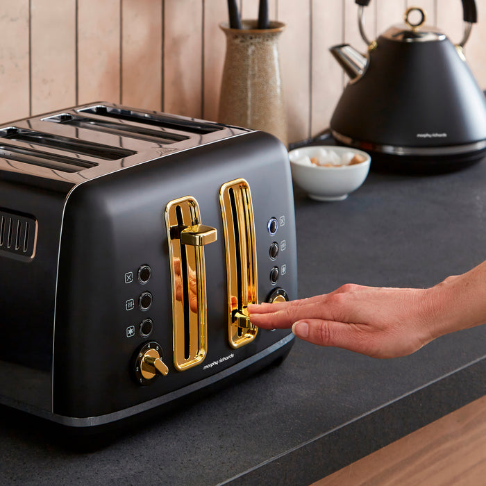 Black toaster with gold accents on a kitchen counter, being operated by a hand.