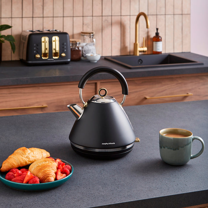 Black kettle on a kitchen counter with a mug and plate of food.