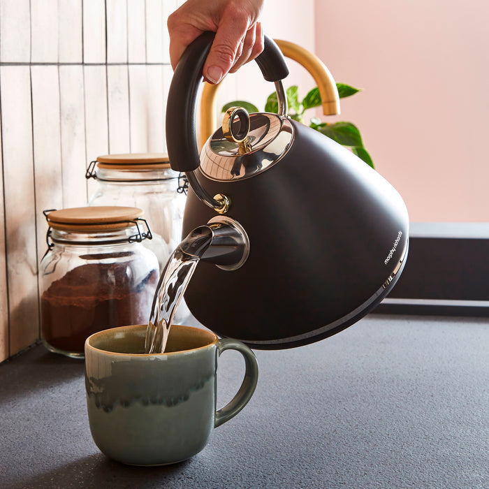 Black kettle being used to pour water into a mug on a kitchen counter.
