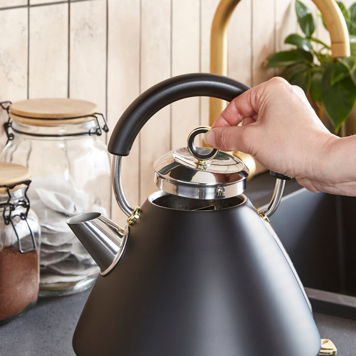 Person opening a black kettle with a kitchen setting in the background