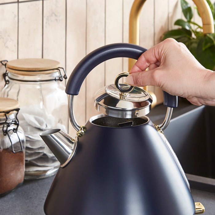 Hand opening a blue kettle with jars and a plant in the background