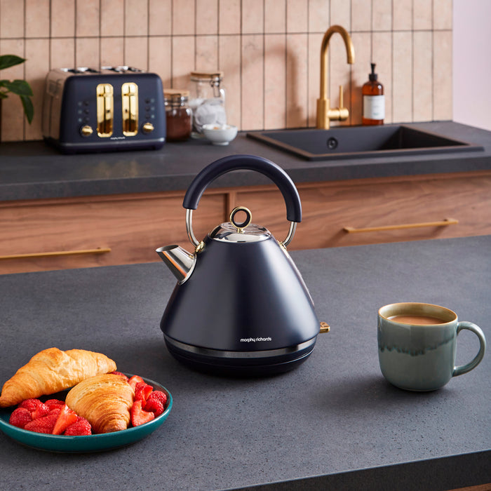 Blue kettle on a kitchen counter with a plate of food and a mug.