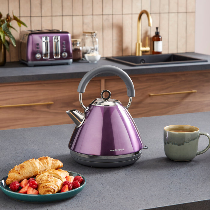 Purple kettle on a kitchen counter with a mug and plate of food.