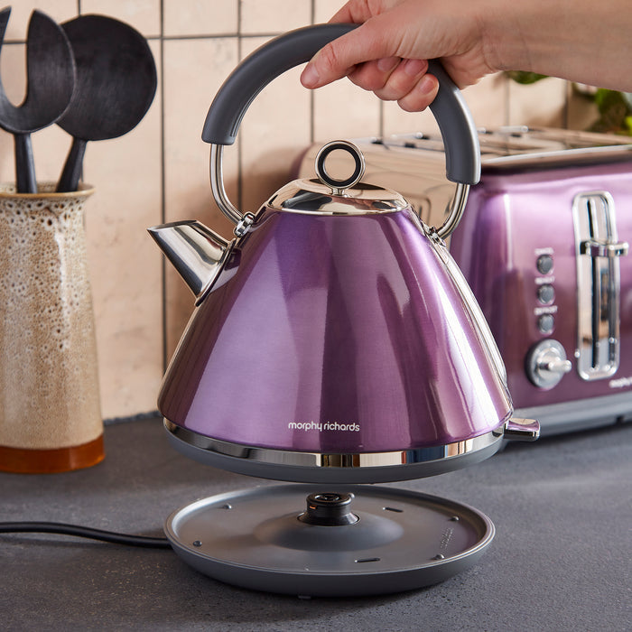 Purple kettle with silver accents being held by a hand on a kitchen counter.