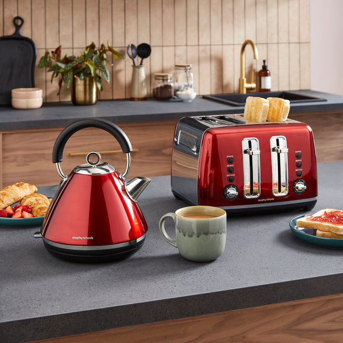 Red kettle and toaster on a kitchen counter with a cup of coffee and breakfast items.