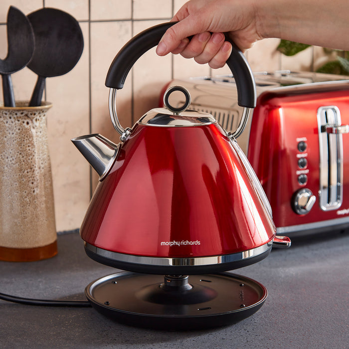 Red Morphy Richards kettle being held with a toaster in the background on a kitchen counter.