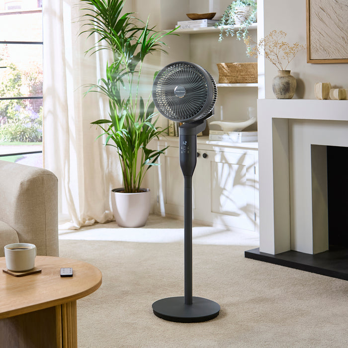 Black stand fan in a living room setting with a plant and table.