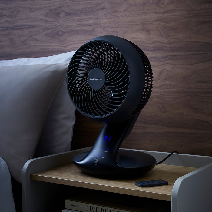 Black fan on a wooden side table with a blurred background