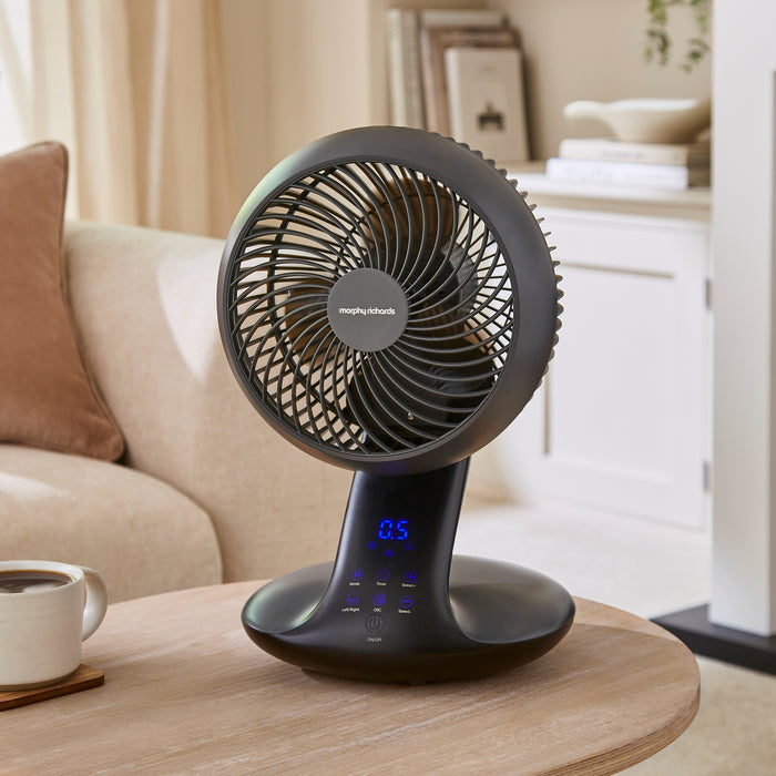 Black table fan on a wooden table with a blurred living room background