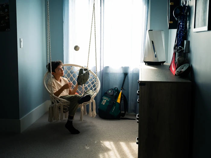 Person sitting in a wicker chair in a room with musical instruments and sports equipment and airdog air purifier.