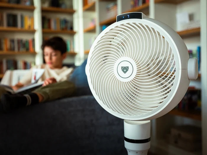 White oscillating Airdog fan in a room with bookshelves and a person reading.