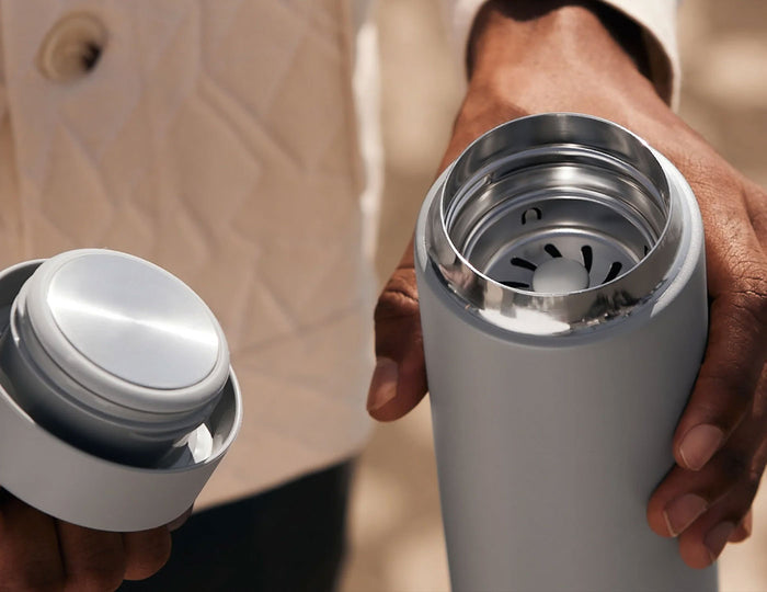 Holding a Carter Infuser Set 16oz Matte White in one hand, and holding lid in the other